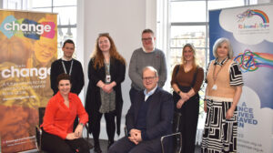 Seven people in the photo posing for a photo. 5 standing at the back and 2 sitting at the front. Two pop up banners at each side of the people - one for Change Mental Health and the other for Richmond's Hope.