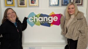two women - Lorna and Sarah-Jayne - with change mental health sign. Lorna has been previously supported by carer support
