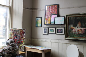 alternative therapy representation: man in headphones painting with a wall exhibition of art work behind him