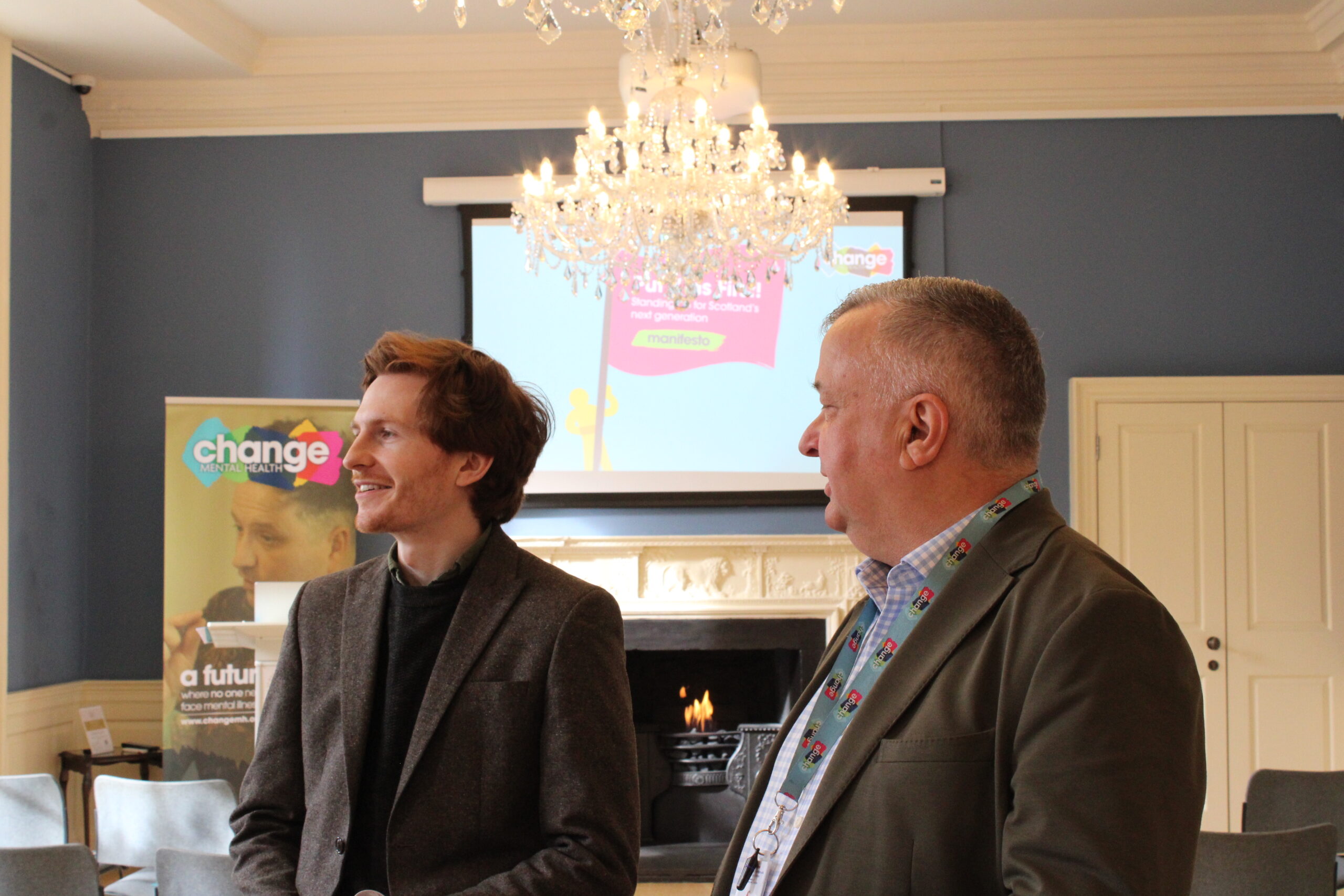 two man standing in conversation with change mental health banner in the background: Jamie Grant(Policy and Public Affairs Manager) and Jim Hume (Director of Public Affairs and Communication) - symbolising mental health policy influencing in Scotland