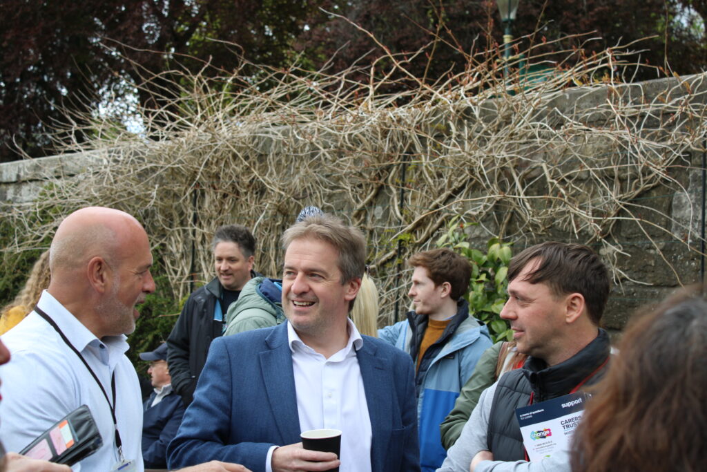 Group of adults chatting and smiling (representatives of Fife Council and in the middle MP Greame Downie) at an outdoor event, with a man in a blue blazer holding a cup in the foreground.
