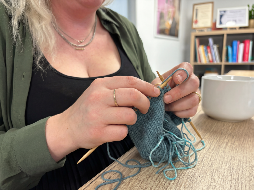 Women in green shirt and black top knitting and blue hat. Sylvia’s story: “I am more than a carer.” - lived experience of a carer and caring impact on mental health. There's support in Tayside!