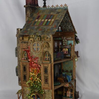 Elaborate multi-story wooden dollhouse with ivy, colorful roof shingles, and visible interior rooms.
