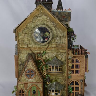 Detailed miniature stone house with a green arched door, round window, and multiple chimneys in a whimsical design.