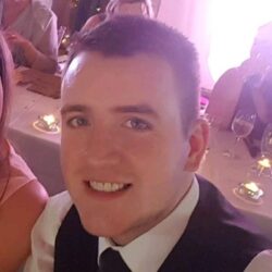 Craig Dundas - Man in a suit and tie smiling at a formal event, seated at a candlelit table.