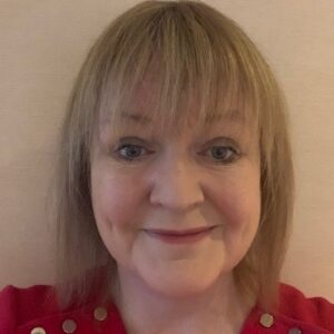 Fiona McAslan - Portrait of a smiling woman with short blonde hair wearing a red sweater against a beige background