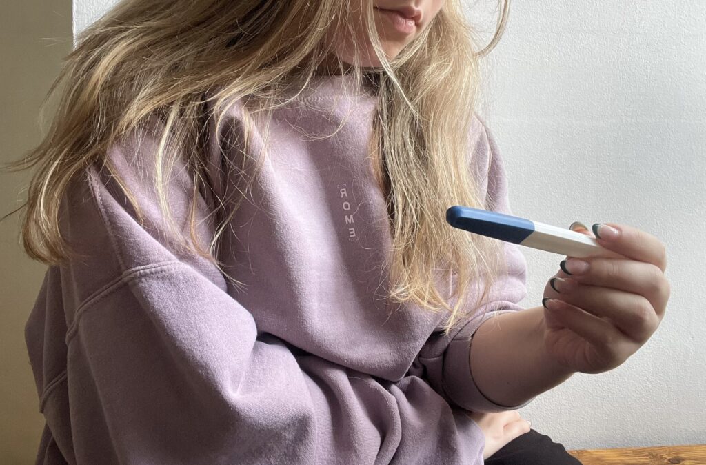 Person with long blond hair wearing a lavender hoodie, holding a blue-capped marker near their chest.