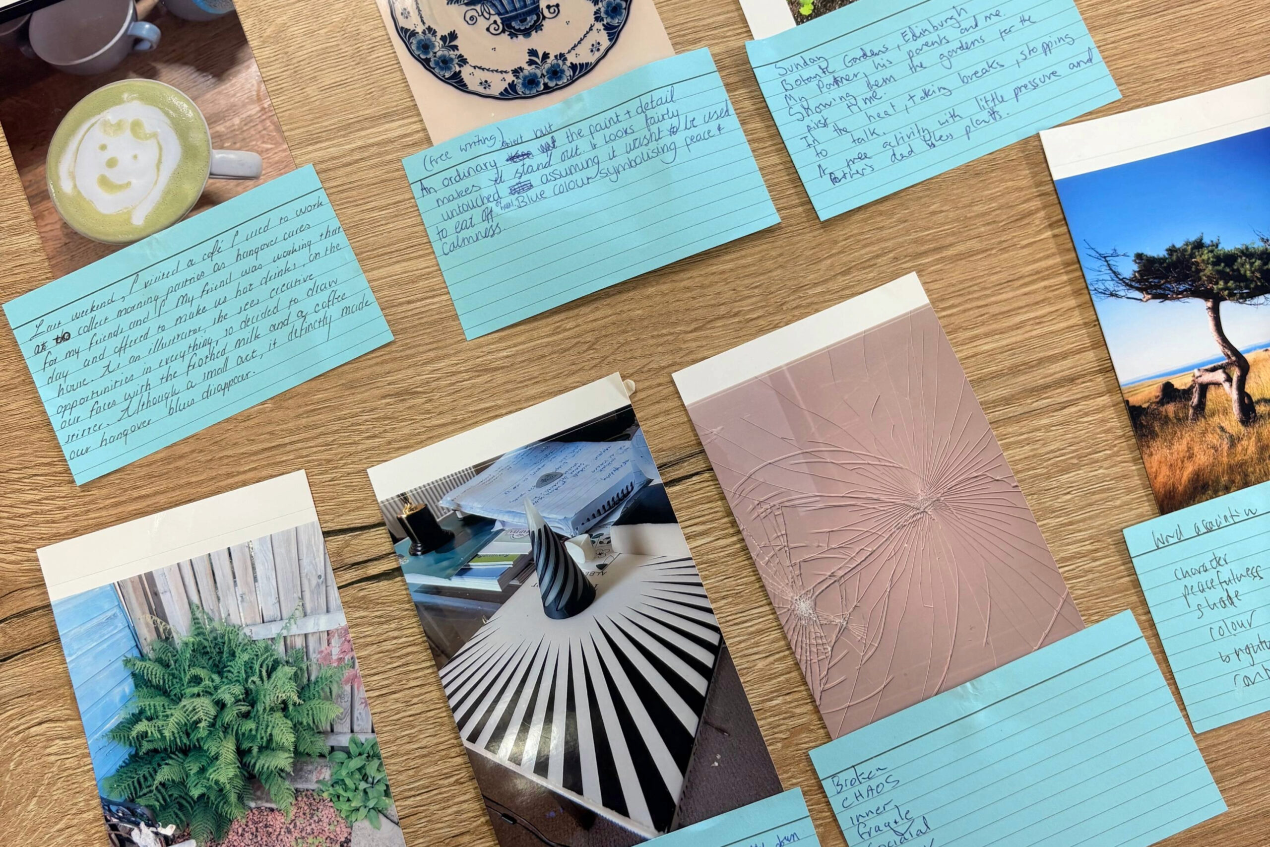 Blue lined notecards with handwritten text laid out on a wooden table, surrounded by cups and photos (plates and flowers).